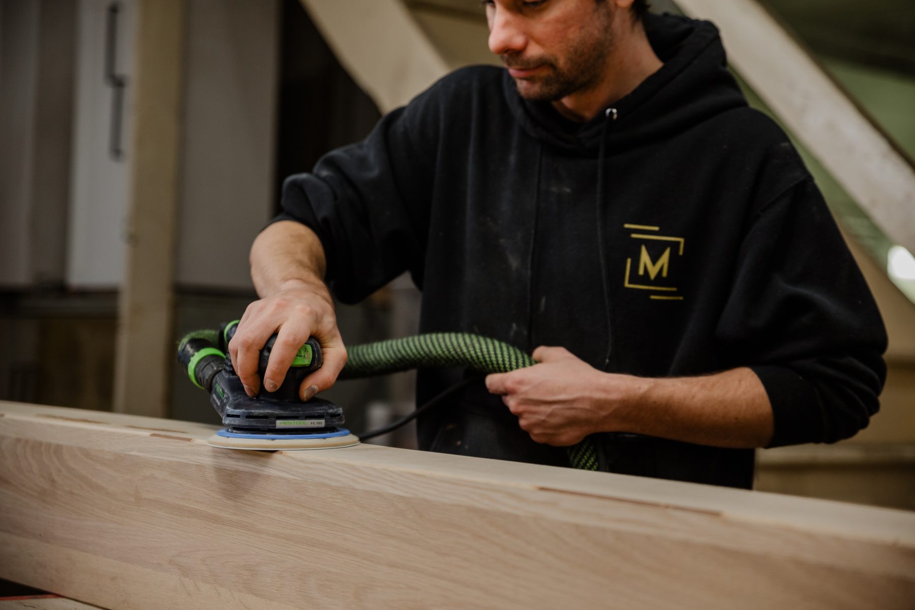 Ébéniste ponçant un plateau de bois massif à l'atelier